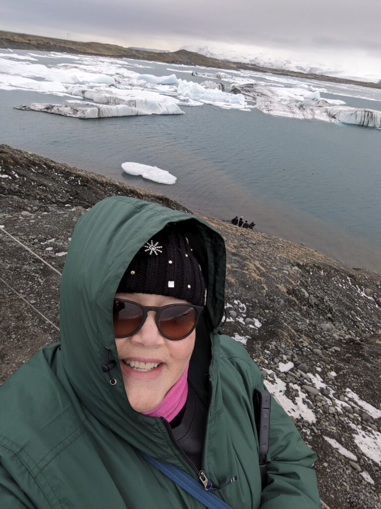 A woman in a green jacket and sunglasses taking a selfie